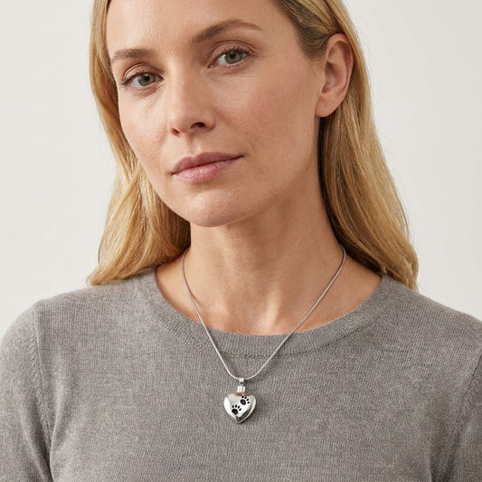 Aramat Jewels zilverkleurige hartvormige ashanger met pootafdrukken, gedragen door een vrouw met blond haar.