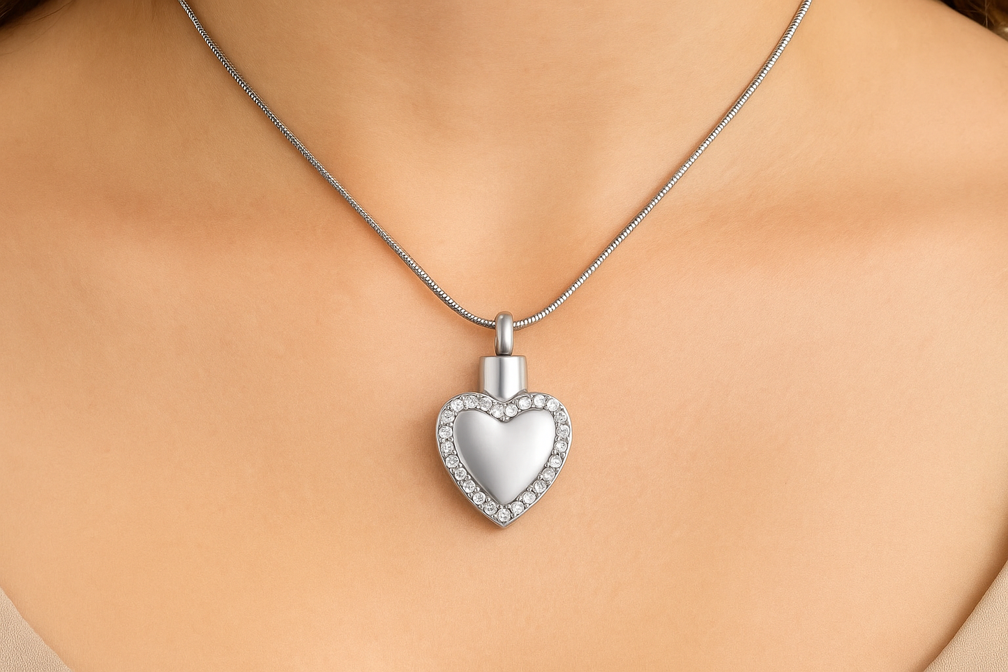 Zilveren hartvormige ashanger met diamanten rand, 33x20mm, gedragen op vrouwenhals met zilveren slangenketting. Luxe gedenksieraad voor asresten, rouwsieraad in hartvorm met kristallen.
