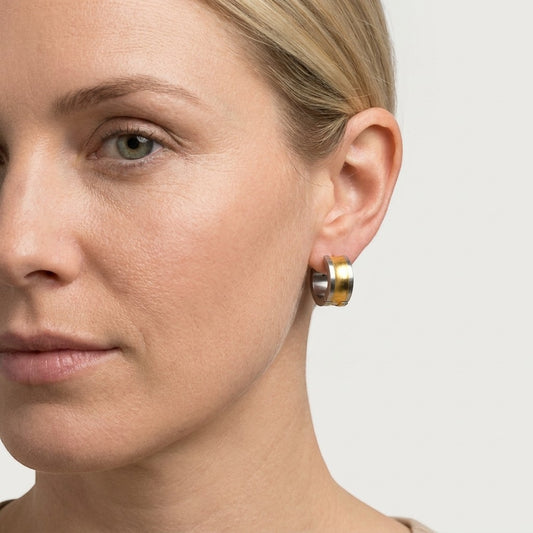 Aramat Jewels bicolor stainless steel hoop earrings with a wide gold stripe, 13mm diameter, worn by a model.