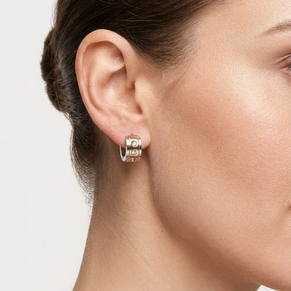 Aramat Jewels bicolor stainless steel huggie hoop earrings with three clear cubic zirconia stones on a woman's ear.