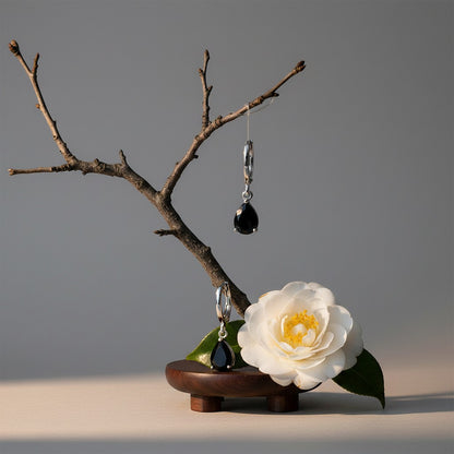 Aramat Jewels silver-tone mini hoop earrings with black teardrop zirconia stones, displayed on a branch with a white flower.