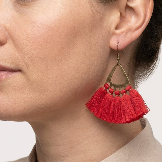 Aramat Jewels boho oorhangers met rode kwastjes en bronskleurige metalen details gedragen door een model.