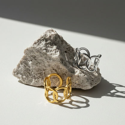 Aramat Jewels brede verstelbare ringen van RVS met ovale schakels in goud- en zilverkleur op een rotsachtige ondergrond