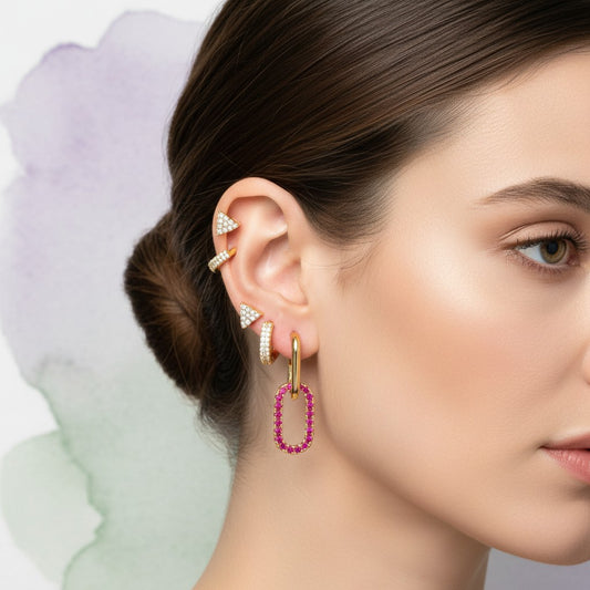 Aramat Jewels gold-plated geometric earring set with triangle studs, oval hoops with pink stones, and small hoops with clear stones.