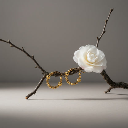 Aramat Jewels gold-tone stainless steel hoop earrings with a beaded pattern and two larger accent beads.