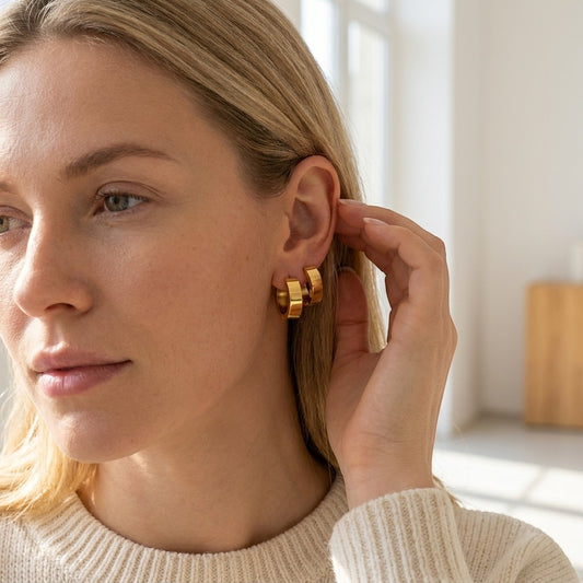 Aramat Jewels gold-colored stainless steel hoop earrings, 20mm diameter, smooth finish, worn by a blonde woman.