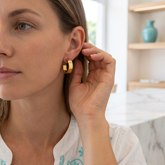 Aramat Jewels gold-tone stainless steel hoop earrings with a small clear cubic zirconia accent, worn by a woman.