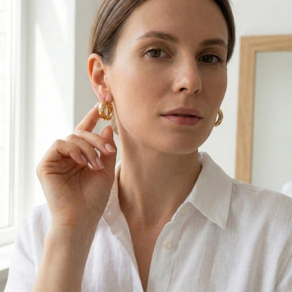 Aramat Jewels gold-tone stainless steel huggie hoop earrings with a central clear cubic zirconia stone.