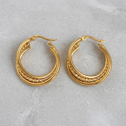 Aramat Jewels triple hoop earrings in gold-tone stainless steel with a twisted design and textured detail, 25mm diameter.