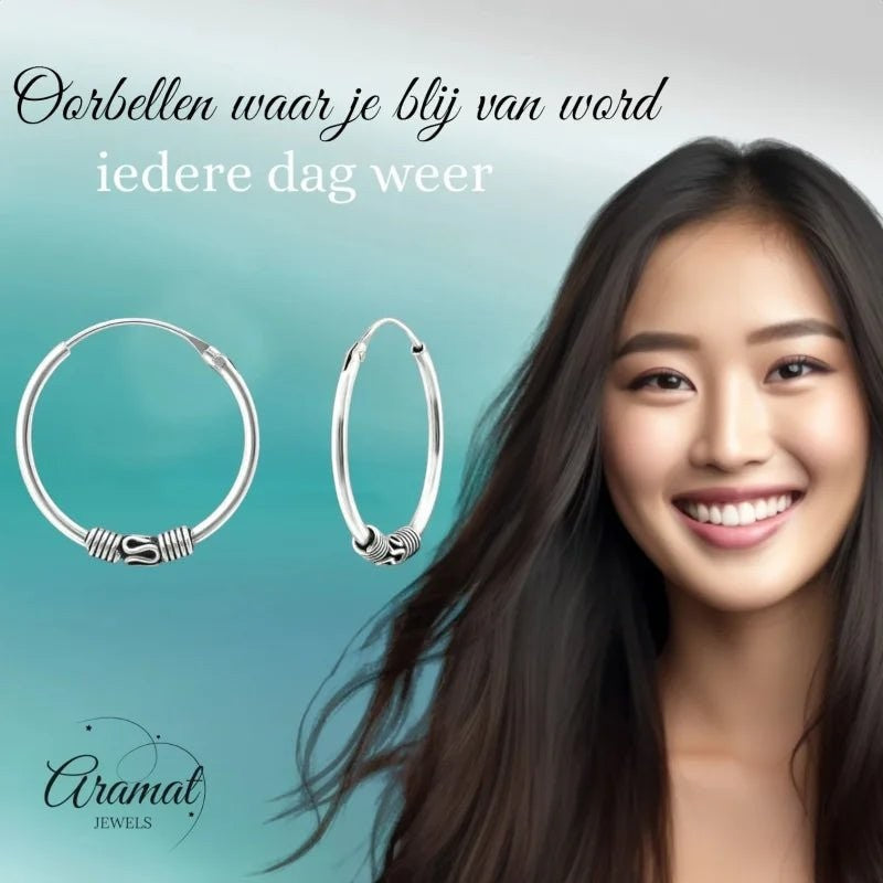 Aramat Jewels oxidised silver Bali hoop earrings, 20mm diameter, with intricate tribal detailing. Model with dark hair smiles.