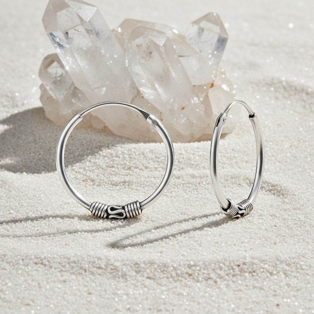 Aramat Jewels 18mm oxidized silver Bali hoop earrings with intricate detailing, styled on a sandy surface with crystals.