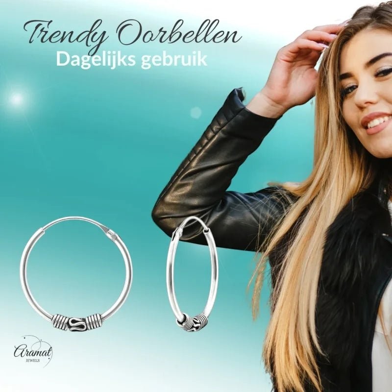 Aramat Jewels oxidized silver Bali hoop earrings, 20mm diameter, with intricate tribal detailing. Model wearing a black leather jacket.