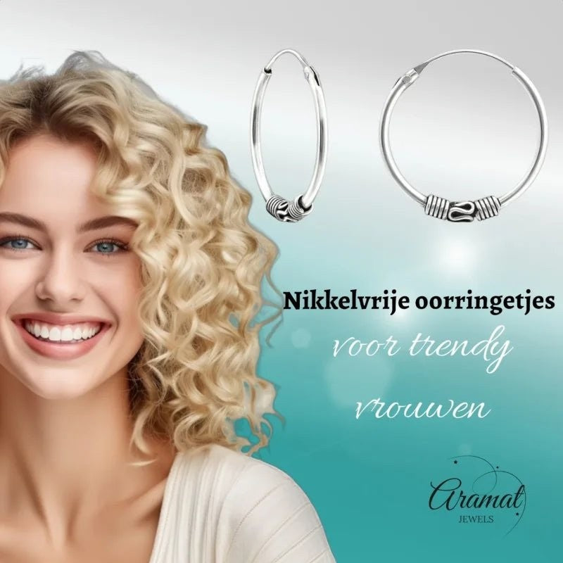 Aramat Jewels 20mm oxidized silver Bali hoop earrings with intricate detailing, worn by a smiling woman with blonde curly hair.