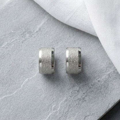 Aramat Jewels sandblasted silver-tone stainless steel huggie hoop earrings, 13mm wide with a textured finish.
