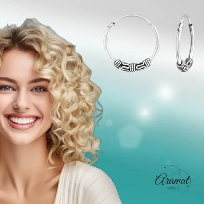 Aramat Jewels unisex 16mm silver Bali hoop earrings with intricate tribal detailing. Model with blonde curly hair smiles.