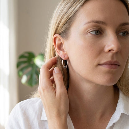 Aramat Jewels 18mm oval silver hoop earrings with intricate ethnic Bali design, worn by a woman.