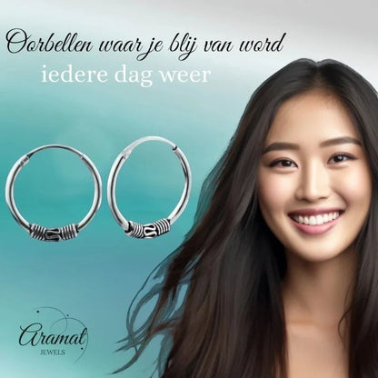 Aramat Jewels unisex 16mm silver Bali hoop earrings with intricate detailing, worn by a smiling young woman.