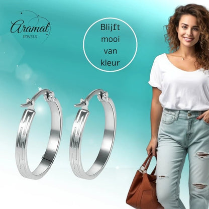 Aramat Jewels silver stainless steel hoop earrings with striped motif, 20mm diameter, worn by a smiling woman in ripped jeans.