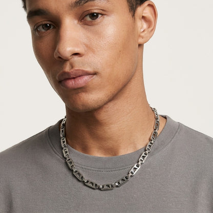 Aramat Jewels brede zilverkleurige stalen koningsketting met kroonmotief gedragen door een man in een grijs shirt.