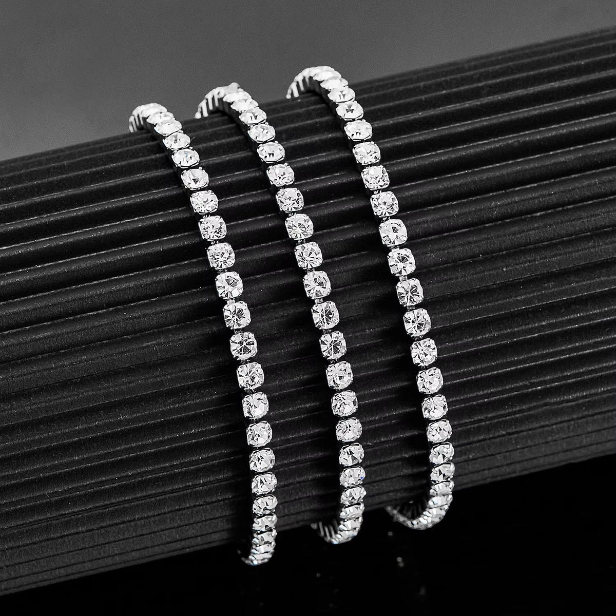 Aramat Jewels zilverkleurige stalen tennisarmband met fonkelende 4mm zirkonia stenen op een zwarte displayhouder.