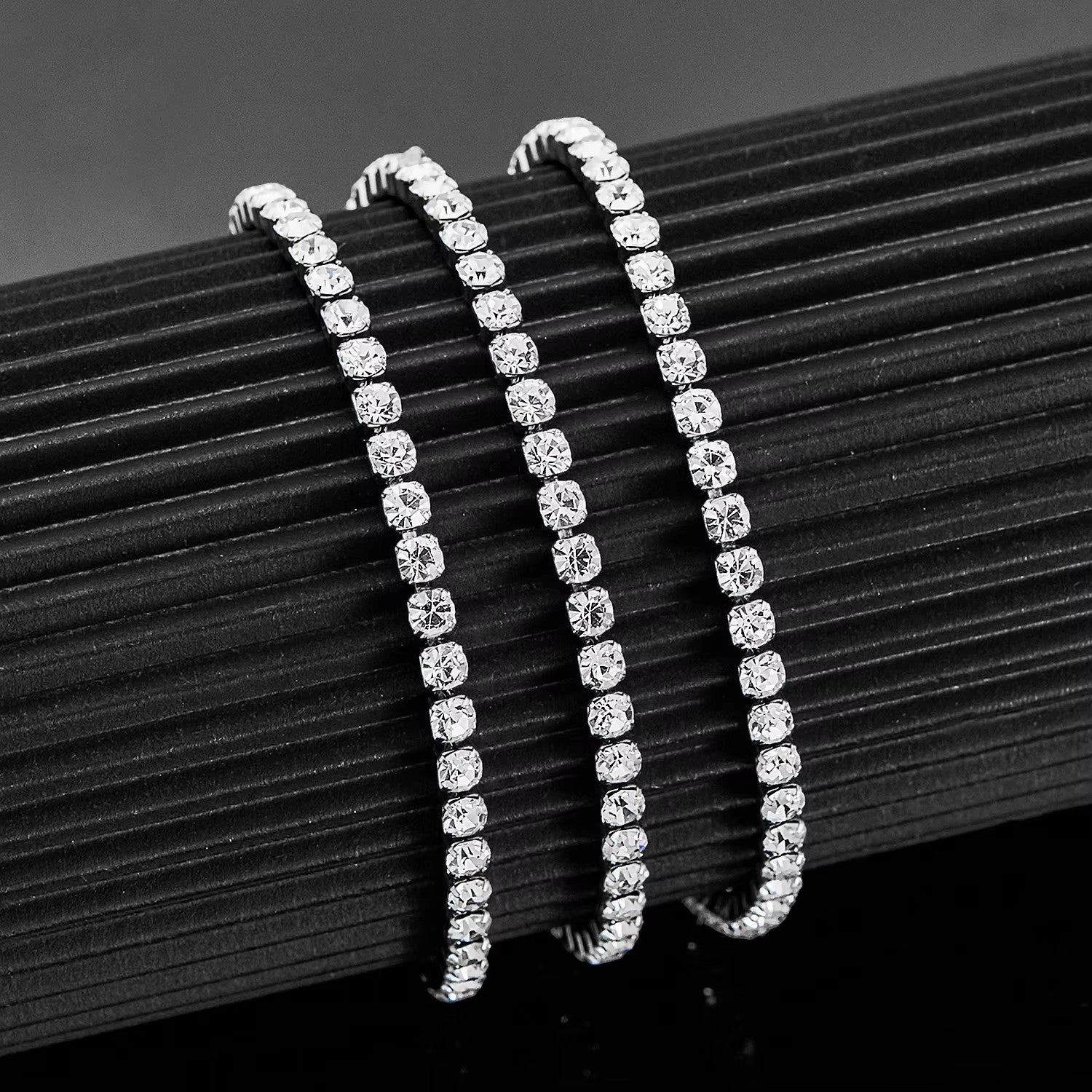 Aramat Jewels zilverkleurige stalen tennisarmband met fonkelende 4mm zirkonia stenen op een zwarte displayhouder.