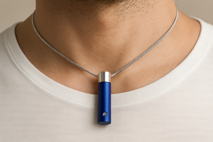 Blauw-zilveren cilindrische ashanger, 36x12mm, met geborsteld blauw metalen lichaam, zilveren dop bovenaan, en kleine diamant accent. De zilveren slangenketting loopt door het midden van de cilinder, gedragen op mannenhals.