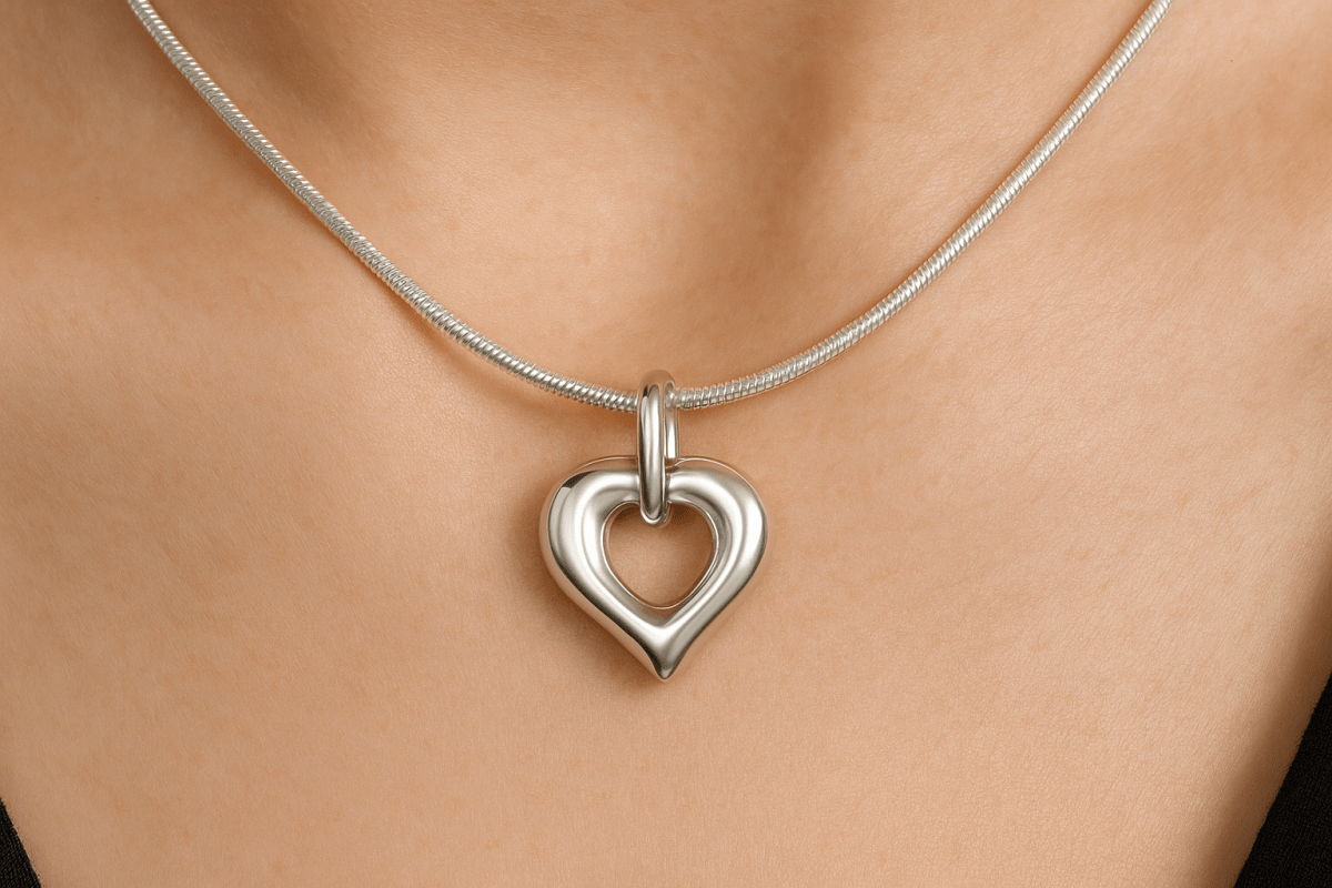 Zilveren open hartvormige ashanger, 25x20mm, met gladde afgeronde randen, puntige onderkant en ovale ring bovenaan, precies zoals het origineel, gedragen op vrouwenhals met zilveren slangenketting.