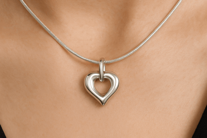 Zilveren open hartvormige ashanger, 25x20mm, met gladde afgeronde randen, puntige onderkant en ovale ring bovenaan, precies zoals het origineel, gedragen op vrouwenhals met zilveren slangenketting.