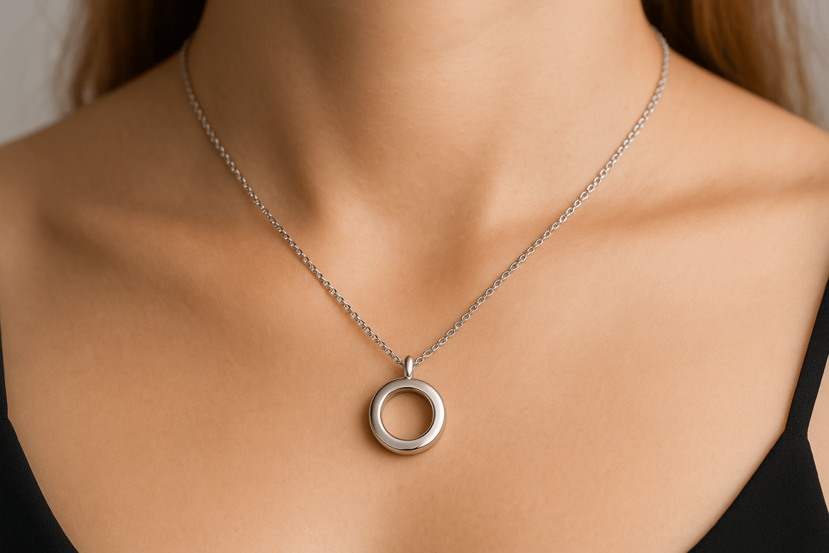 Een ronde RVS ashanger met een diameter van 15mm gedragen om een vrouwelijke hals. De hanger heeft een eenvoudig, elegant ontwerp met een ronde opening in het midden waar as bewaard kan worden.