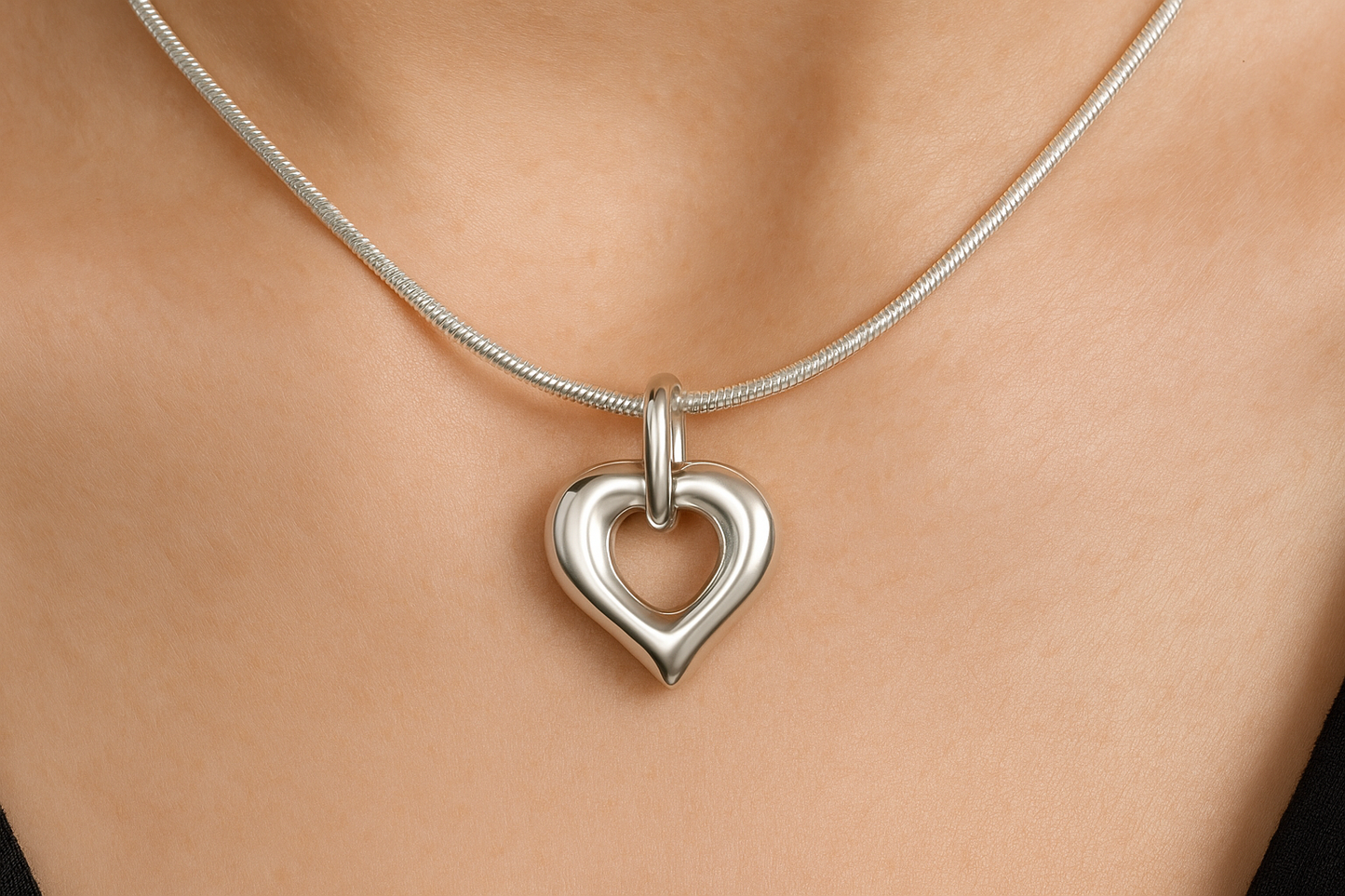 Zilveren open hartvormige ashanger, 25x20mm, met gladde afgeronde randen, puntige onderkant en ovale ring bovenaan, precies zoals het origineel, gedragen op vrouwenhals met zilveren slangenketting.